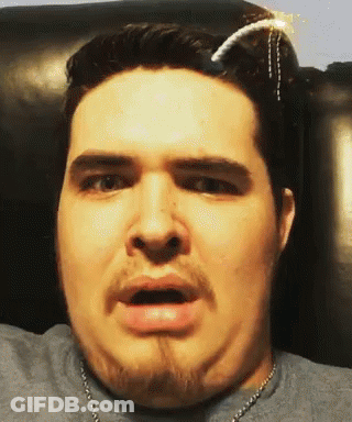 A Man With A Beard Is Wearing A Gray Shirt And A Necklace GIF