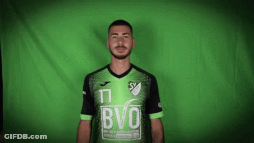 A Man With A Beard Is Wearing A Green And Black Soccer Jersey . GIF