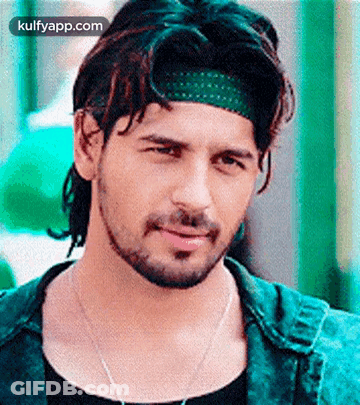 A Man With A Beard Is Wearing A Green Headband And A Black Shirt . GIF