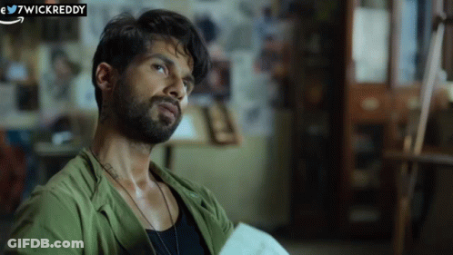 A Man With A Beard Is Wearing A Green Shirt And A Black Tank Top . GIF