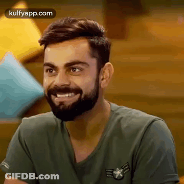 A Man With A Beard Is Wearing A Green Shirt And Smiling . GIF