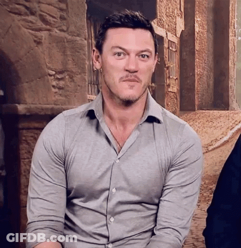 A Man With A Beard Is Wearing A Grey Shirt And Making A Face . GIF