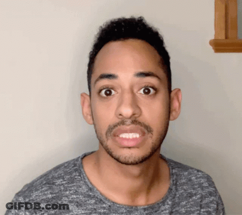 A Man With A Beard Is Wearing A Grey Shirt And Making A Funny Face GIF