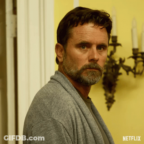 A Man With A Beard Is Wearing A Grey Sweater With A Netflix Logo On The Bottom GIF