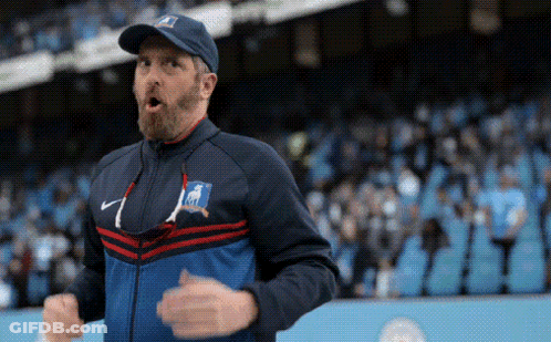 A Man With A Beard Is Wearing A Hat And A Jacket While Standing In Front Of A Crowd . GIF