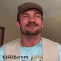A Man With A Beard Is Wearing A Hat And A Vest And Smiling . GIF