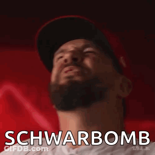A Man With A Beard Is Wearing A Hat And Has The Word Schwarbomb Written On His Face GIF