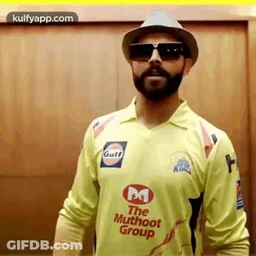 A Man With A Beard Is Wearing A Hat And Sunglasses While Wearing A Yellow Shirt . GIF