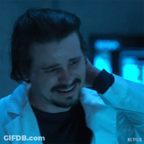 A Man With A Beard Is Wearing A Lab Coat And Smiling While Holding His Neck . GIF