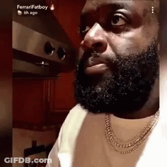 A Man With A Beard Is Wearing A Necklace And Looking At The Camera . GIF