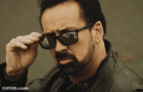 A Man With A Beard Is Wearing A Pair Of Sunglasses With A Reflection Of A Building GIF