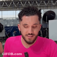 A Man With A Beard Is Wearing A Pink Shirt And Smiling While Holding A Microphone . GIF