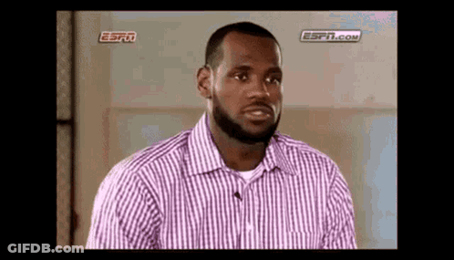 A Man With A Beard Is Wearing A Purple And White Striped Shirt And Talking To A Microphone . GIF