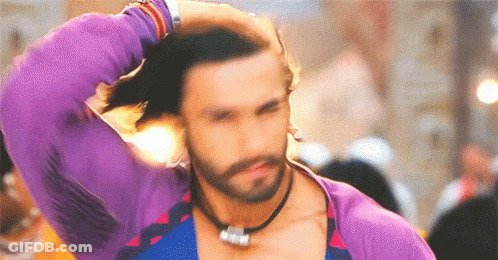 A Man With A Beard Is Wearing A Purple Shirt And A Necklace . GIF