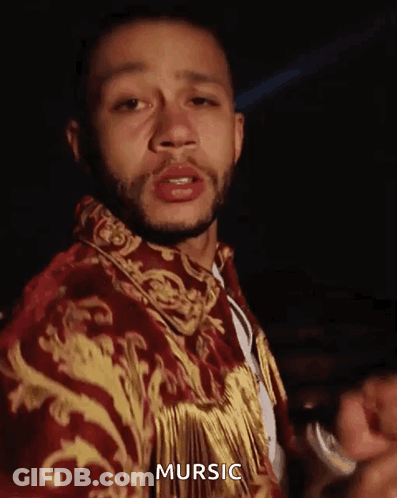 A Man With A Beard Is Wearing A Red And Gold Jacket With The Word Mursic On It . GIF