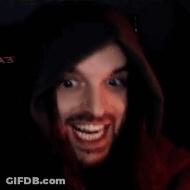 A Man With A Beard Is Wearing A Red Hoodie And Smiling In A Dark Room . GIF