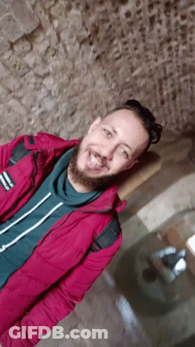 A Man With A Beard Is Wearing A Red Jacket That Says Reebok GIF