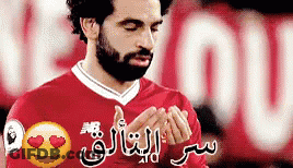 A Man With A Beard Is Wearing A Red Jersey With Arabic Writing On It GIF