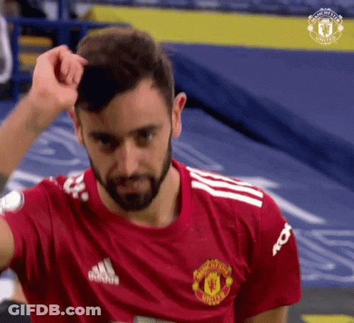 A Man With A Beard Is Wearing A Red Manchester United Jersey And Adjusting His Hair . GIF