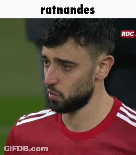 A Man With A Beard Is Wearing A Red Shirt And Making A Funny Face On A Soccer Field . GIF