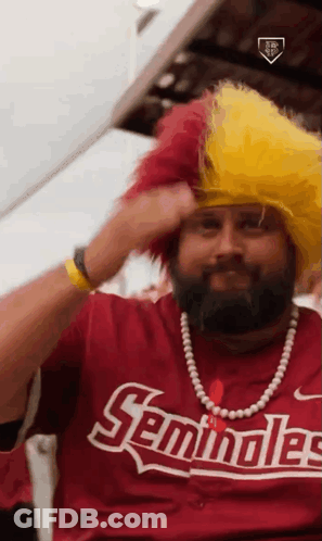 A Man With A Beard Is Wearing A Seminoles Shirt And A Yellow Wig GIF