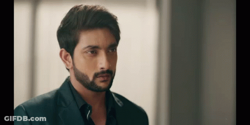 A Man With A Beard Is Wearing A Suit And Black Shirt And Looking At The Camera . GIF