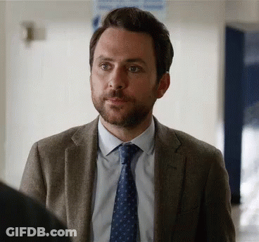 A Man With A Beard Is Wearing A Suit And Tie And Looking At Something . GIF