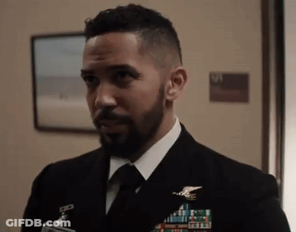 A Man With A Beard Is Wearing A Suit And Tie And Standing In A Hallway . GIF