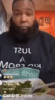 A Man With A Beard Is Wearing A T2ul Hoodie And Holding A Plate Of Food . GIF