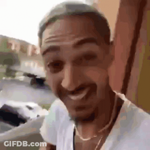 A Man With A Beard Is Wearing A White Shirt And A Gold Chain Around His Neck . GIF