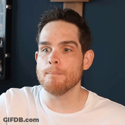 A Man With A Beard Is Wearing A White Shirt And Looking At The Camera GIF