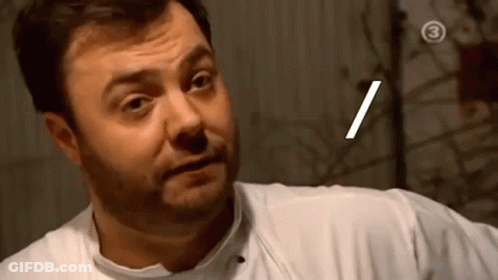 A Man With A Beard Is Wearing A White Shirt And Making A Face . GIF