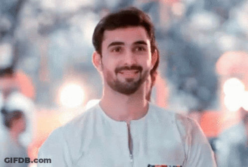 A Man With A Beard Is Wearing A White Shirt And Smiling For The Camera . GIF