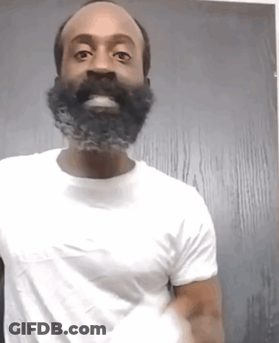 A Man With A Beard Is Wearing A White Shirt And Smiling GIF