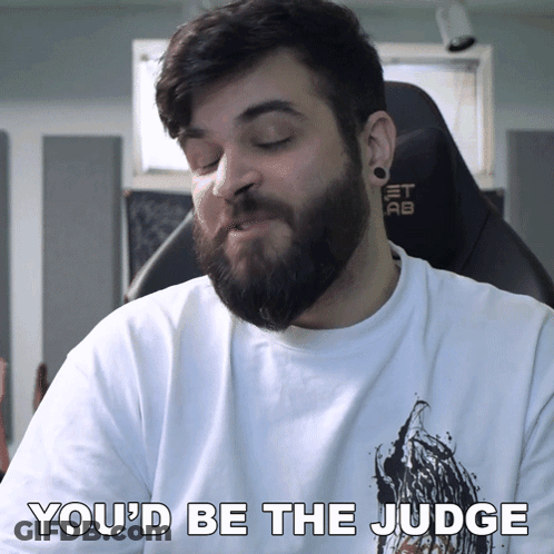 A Man With A Beard Is Wearing A White Shirt That Says " You 'D Be The Judge " GIF
