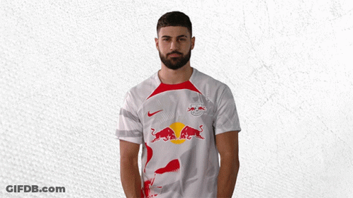 A Man With A Beard Is Wearing A White Shirt With A Red Bull On It GIF