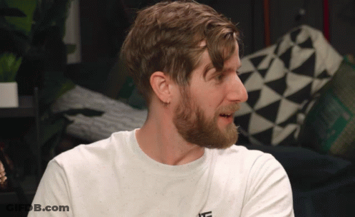 A Man With A Beard Is Wearing A White T-Shirt With The Letter L On The Front GIF