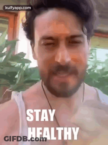 A Man With A Beard Is Wearing A White Tank Top And A Necklace . GIF