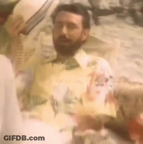 A Man With A Beard Is Wearing A Yellow Shirt And A Hat GIF