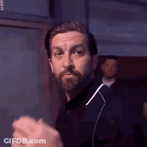 A Man With A Beard Is Wearing Ear Buds And Making A Funny Face . GIF