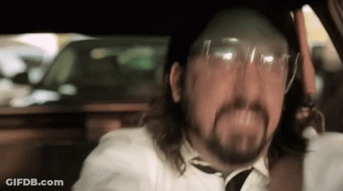 A Man With A Beard Is Wearing Glasses And A Tie While Driving A Car . GIF