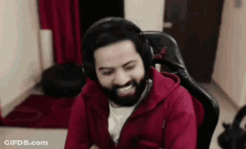A Man With A Beard Is Wearing Headphones And A Red Jacket While Sitting In A Chair . GIF