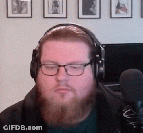 A Man With A Beard Is Wearing Headphones And Glasses While Sitting In Front Of A Microphone . GIF