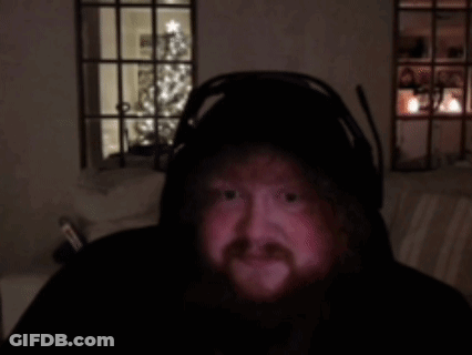 A Man With A Beard Is Wearing Headphones In A Dark Room With A Christmas Tree In The Background GIF
