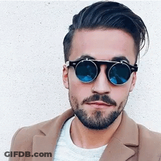 A Man With A Beard Is Wearing Sunglasses And A Coat . GIF