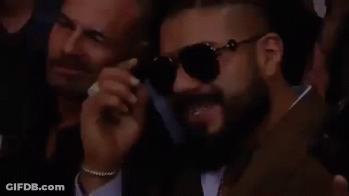 A Man With A Beard Is Wearing Sunglasses While Sitting In A Crowd Of People . GIF