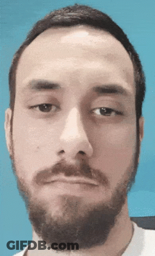 A Man With A Beard Looks At The Camera With A Blue Background GIF