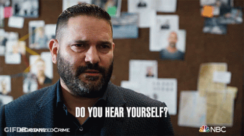A Man With A Beard Says " Do You Hear Yourself " In Front Of A Wall Of Pictures GIF