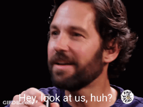A Man With A Beard Says Hey Look At Us Huh In Front Of A Black Background GIF