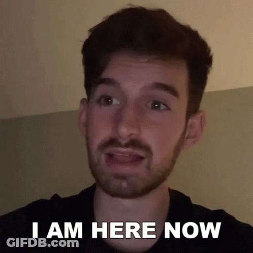 A Man With A Beard Says " I Am Here Now " In Front Of His Face GIF